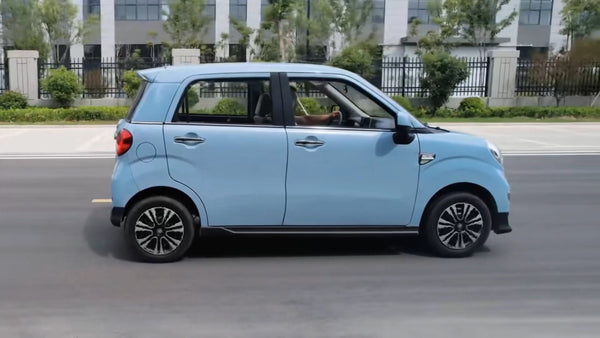 Small blue Wink Mark3 LSV driving on a road with buildings and greenery in the background